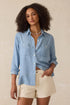 Woman wearing a light blue denim shirt and beige shorts against a neutral background