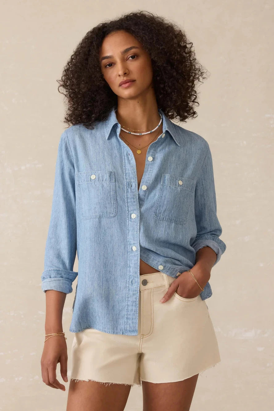 Woman wearing a light blue denim shirt and beige shorts against a neutral background