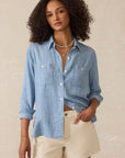Woman wearing a light blue denim shirt and beige shorts against a neutral background