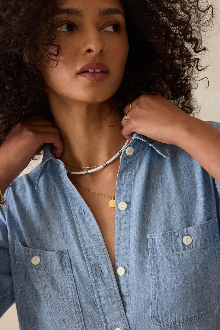 Woman wearing a blue denim shirt with visible jewelry on a neutral background