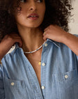 Woman wearing a blue denim shirt with visible jewelry on a neutral background