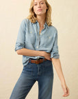 Woman wearing a light blue denim shirt and jeans on a beige background