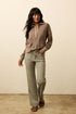 Woman wearing a brown sweater and beige pants against a plain background