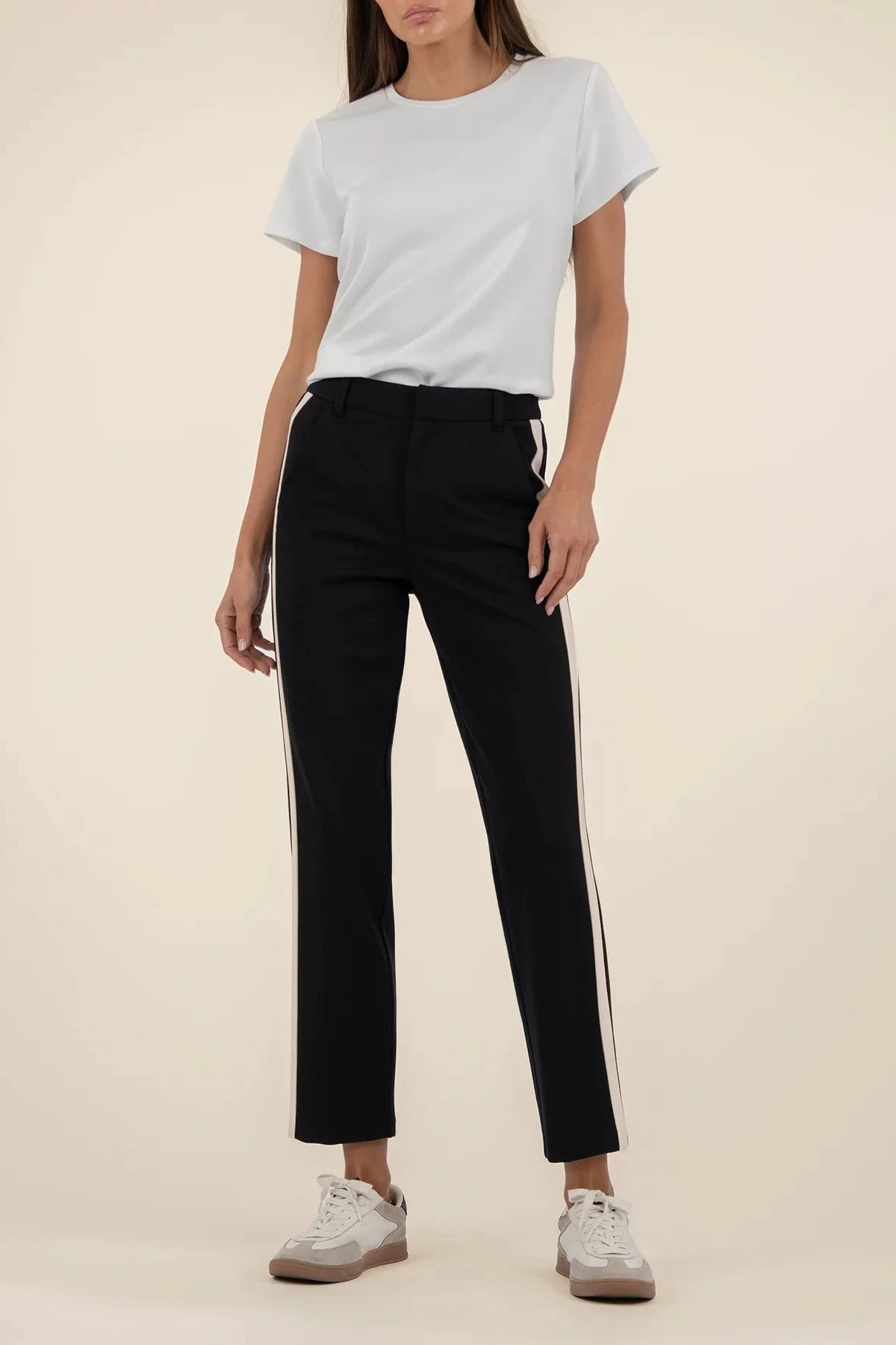 Person wearing a light gray t-shirt and black pants with white stripes on a beige background