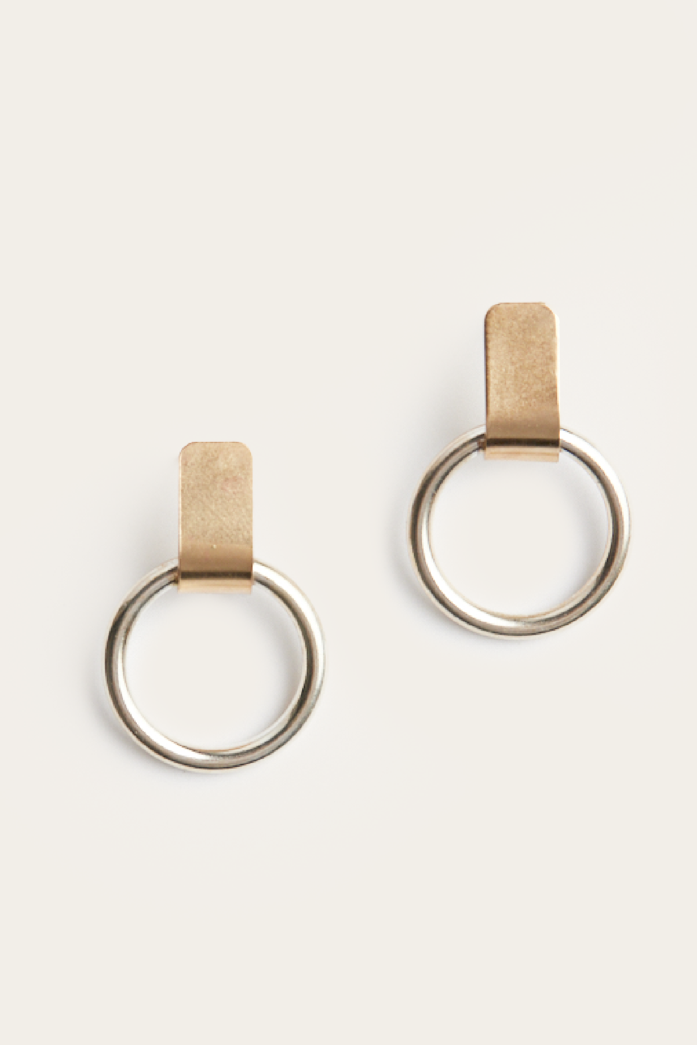 Pair of gold hoop earrings with leather straps on a beige background