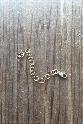 A gold-colored necklace extender laid out on a wooden surface.