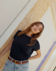 Woman wearing a black t-shirt and blue jeans standing against a textured wall.