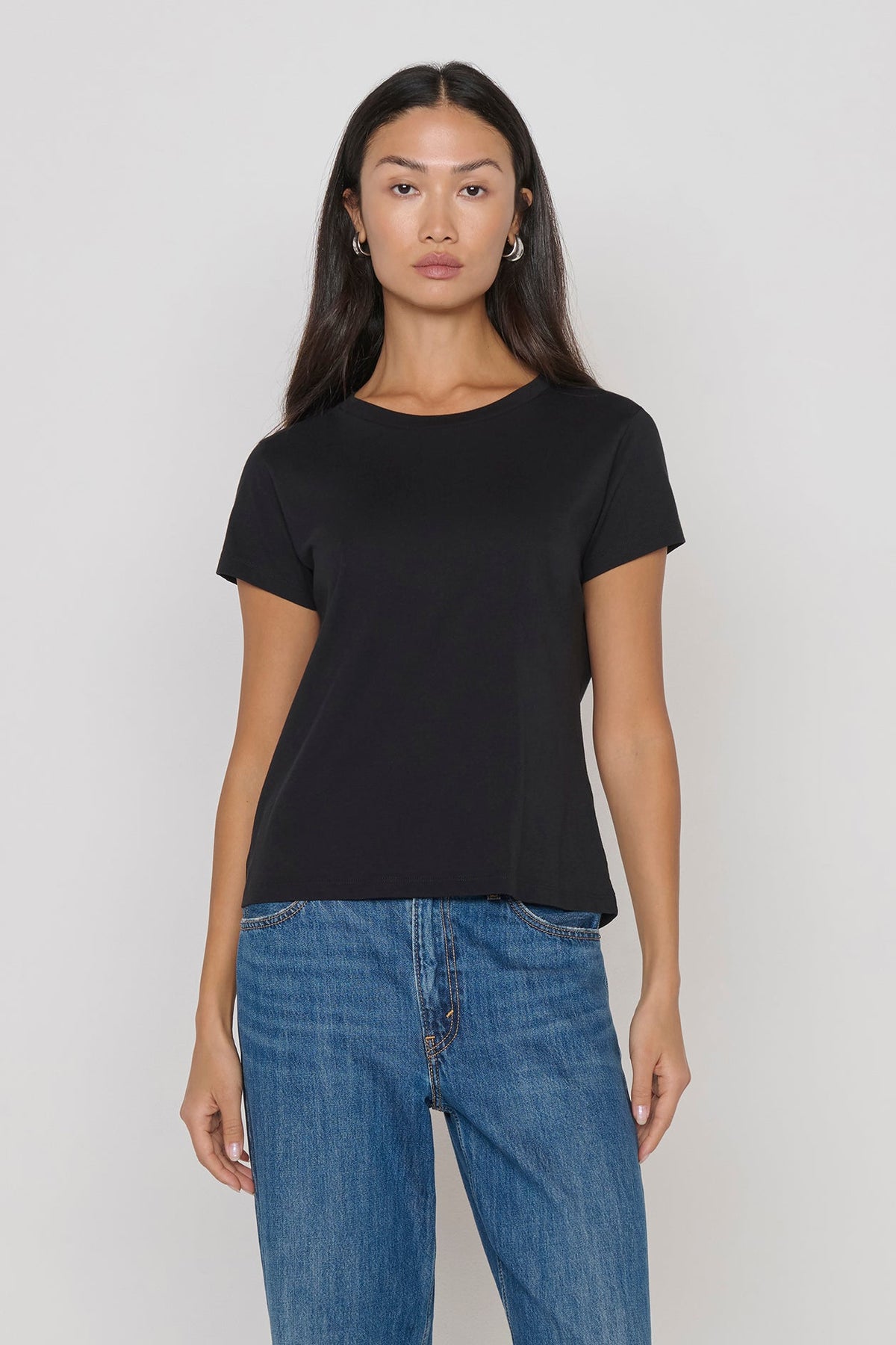 Woman wearing a black t-shirt and blue jeans against a plain background