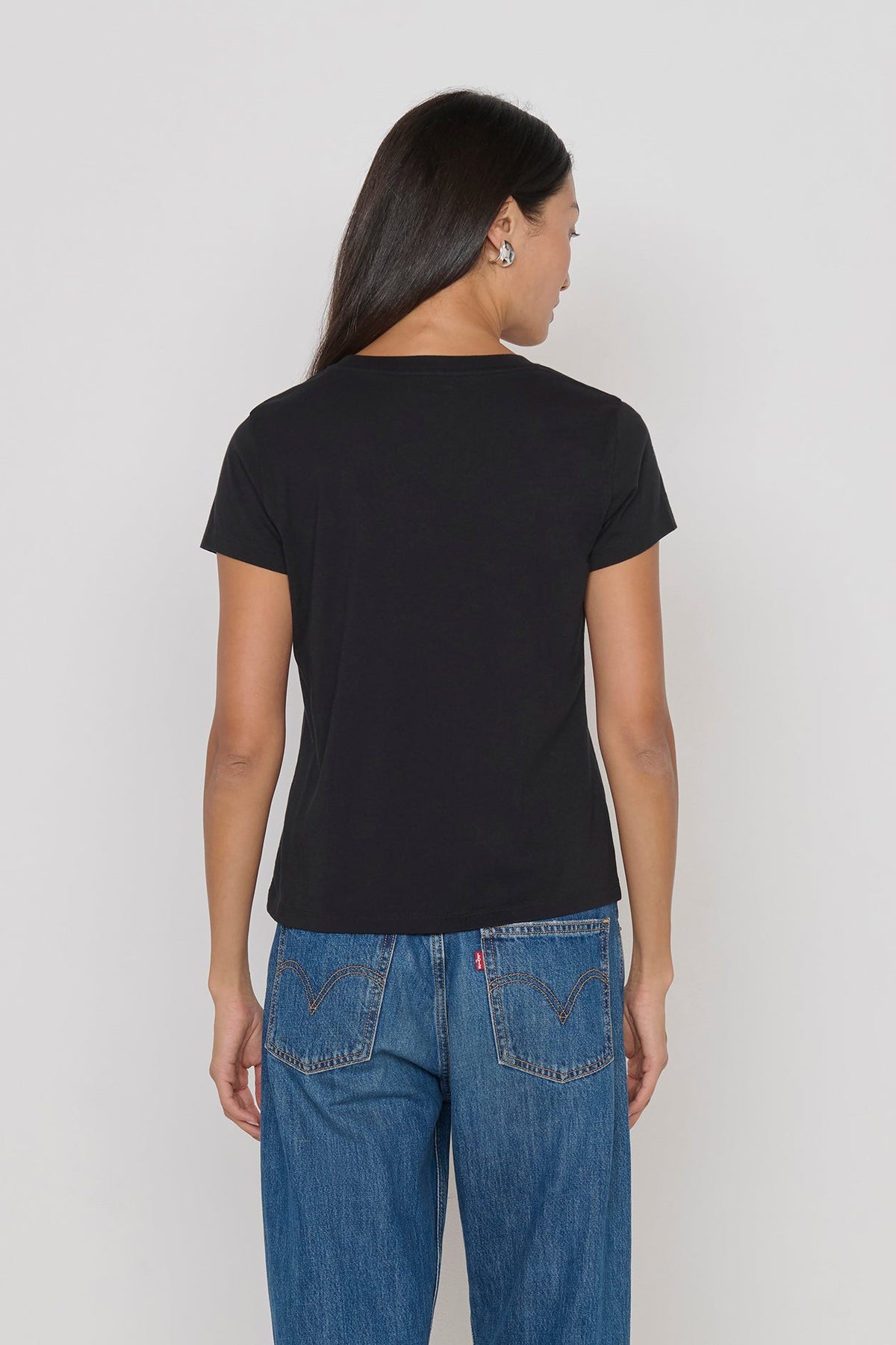 Person wearing a black t-shirt and blue jeans on a plain background