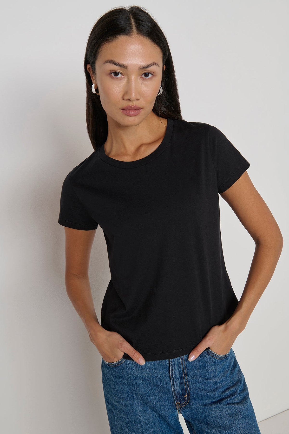 Woman wearing a black t-shirt and blue jeans against a plain background