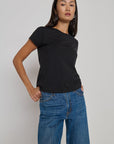 A woman modeling a black short-sleeve crewneck t-shirt paired with blue jeans, standing against a plain light gray studio background.