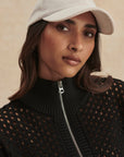 Woman wearing a beige cap and black textured sweater with a zipper.