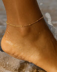 Close-up of a foot with a gold anklet on a beach