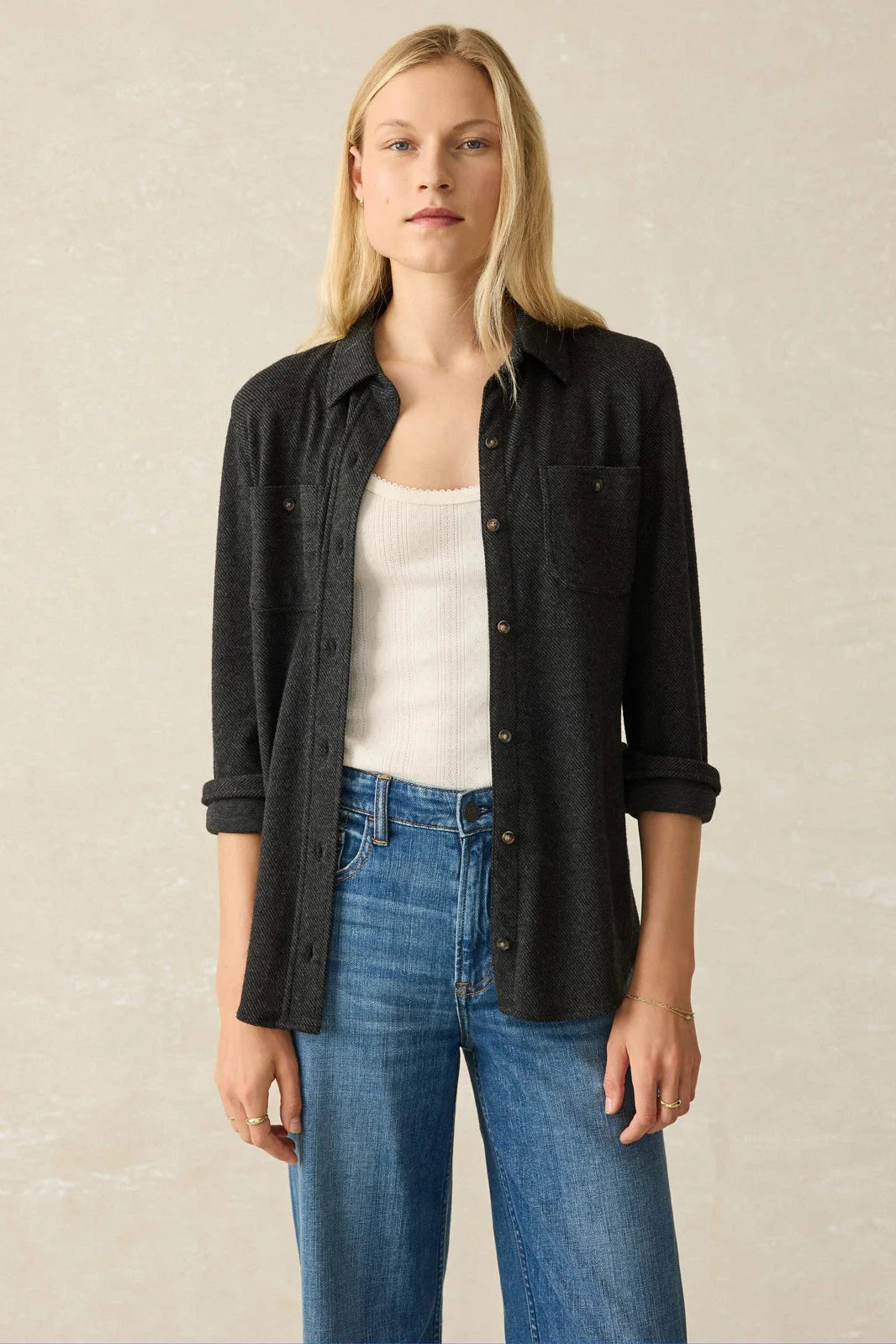 Woman wearing a black shirt, white top, and blue jeans against a beige background