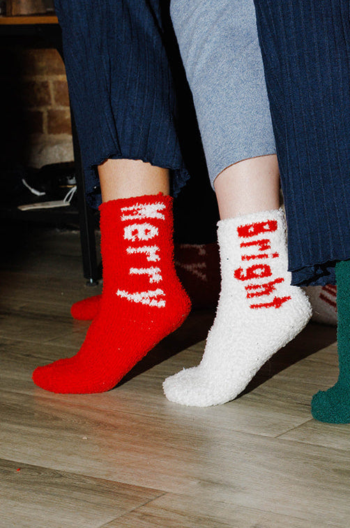 Four pairs of feet wearing colorful socks with text, standing on a wooden floor.