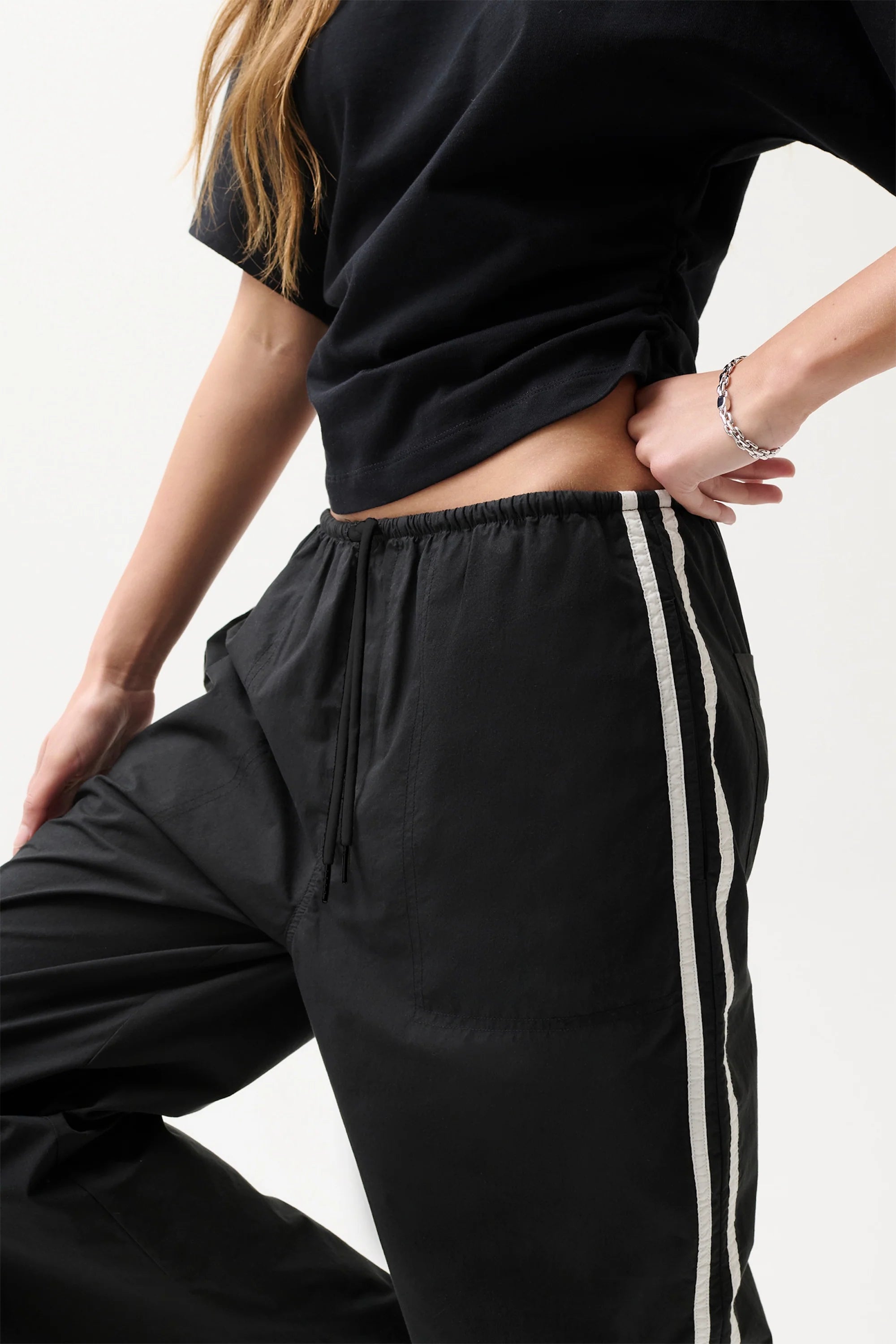 Person wearing black jogger pants with a white stripe on a light background