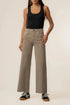 A model wearing a pair of high-waisted, wide-leg taupe jeans, paired with a black tank top and black sneakers, standing against a plain off-white studio background.