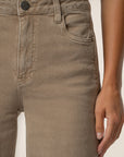 Close-up of a person wearing light brown or taupe denim jeans, showing the front waistband, button, belt loops, right pocket, and hand resting near the thigh.