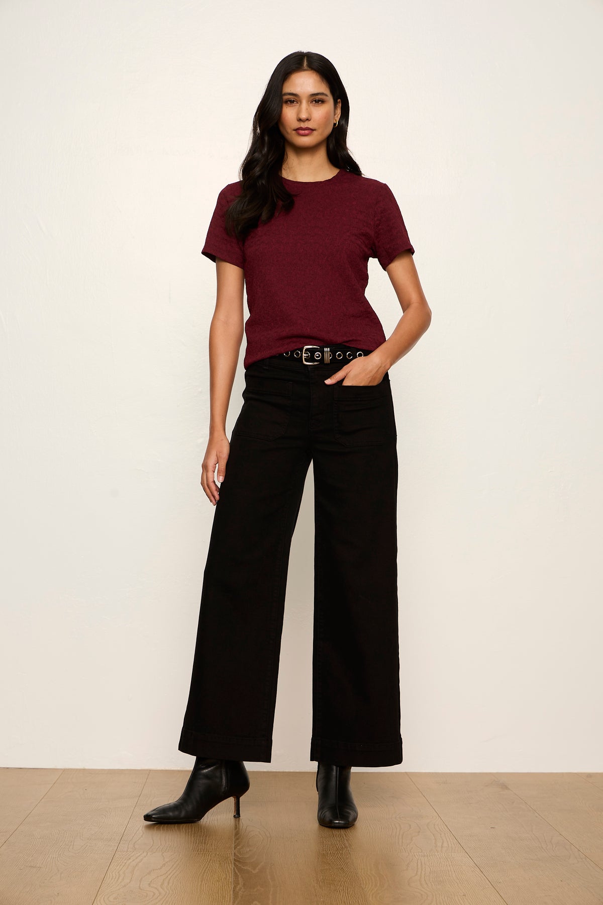 Woman wearing a burgundy t-shirt and black pants against a white background