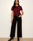 Woman wearing a burgundy t-shirt and black pants against a white background