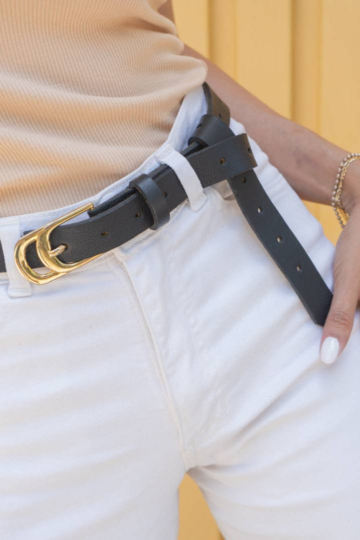 Person wearing a black belt with a gold buckle on white pants against a yellow background