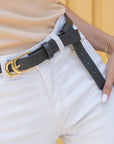 Person wearing a black belt with a gold buckle on white pants against a yellow background
