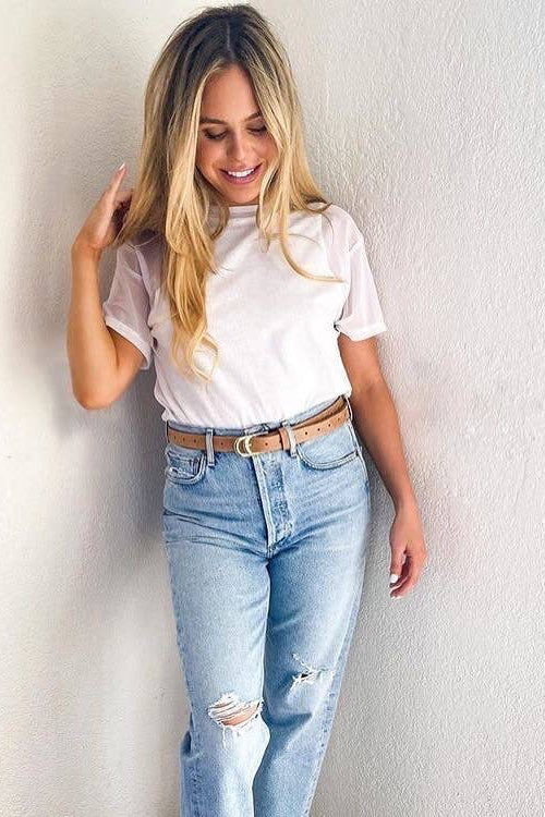 Woman wearing a white t-shirt and light blue jeans against a plain background