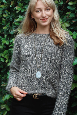 Woman wearing a textured gray sweater with a decorative button against a green leafy background