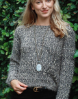 Woman wearing a textured gray sweater with a decorative button against a green leafy background