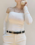 Person wearing a white long-sleeve top and beige pants with a black belt against a plain background