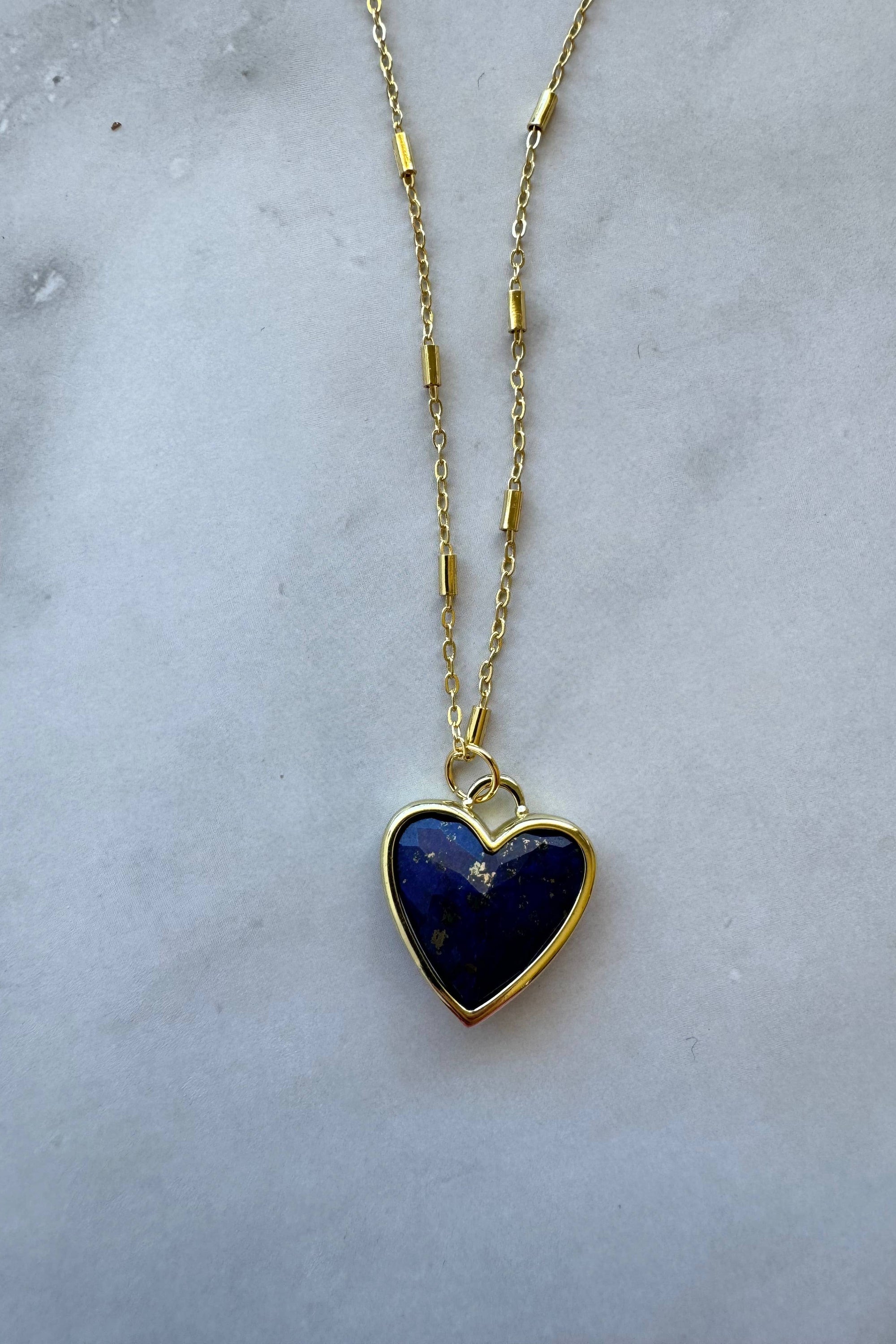 Heart-shaped lapis lazuli pendant on a gold chain against a marble background