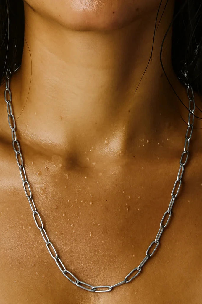 Close-up of a person wearing a silver chain necklace on a neutral background
