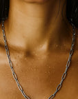 Close-up of a person wearing a silver chain necklace on a neutral background
