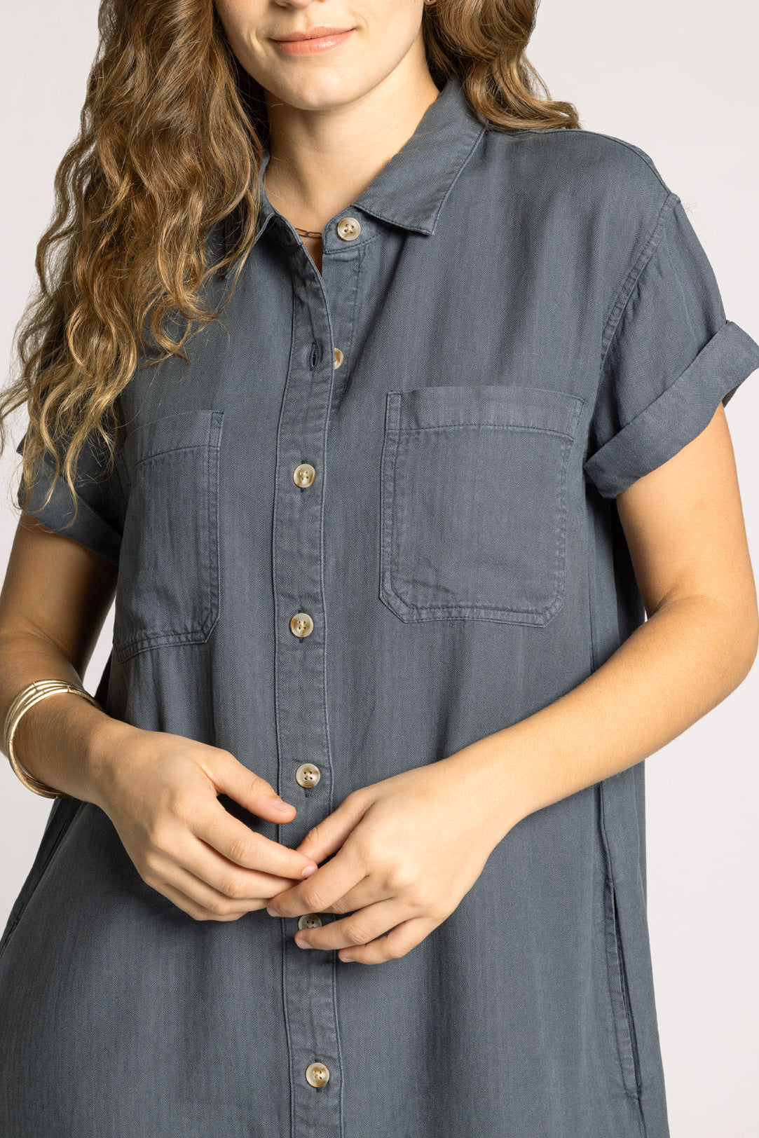 Woman wearing a gray button-up shirt against a plain background