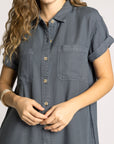 Woman wearing a gray button-up shirt against a plain background