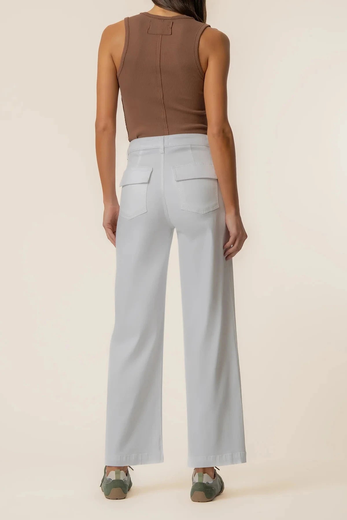 Person wearing a brown sleeveless top and light blue high-waisted pants on a beige background