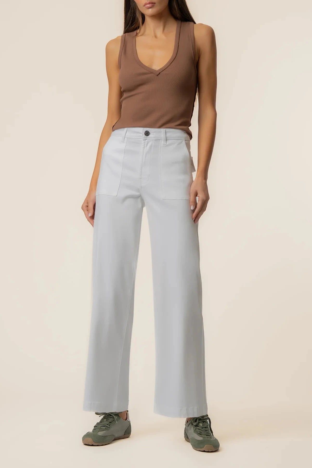 Person wearing a brown tank top and light blue pants on a beige background