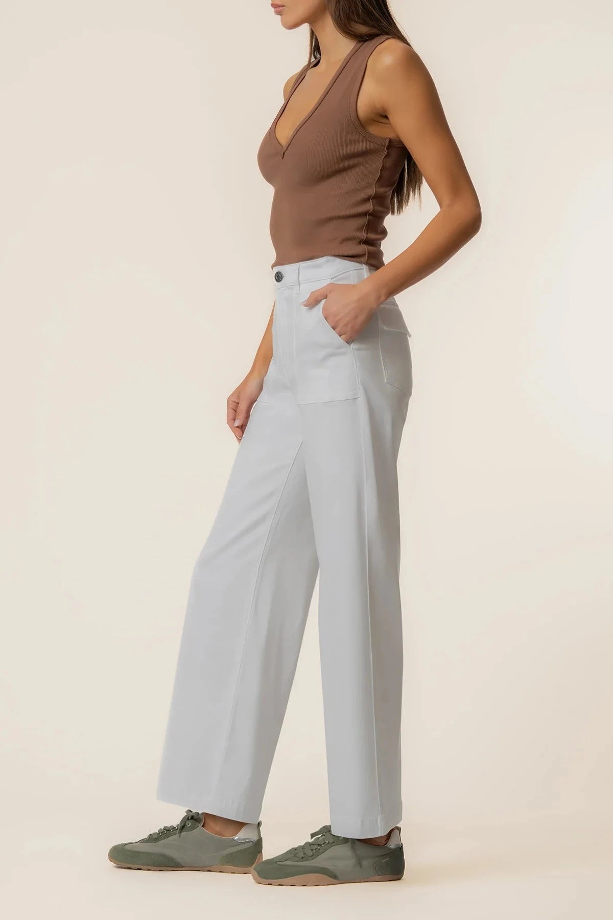 Person wearing light blue pants and a brown top on a beige background