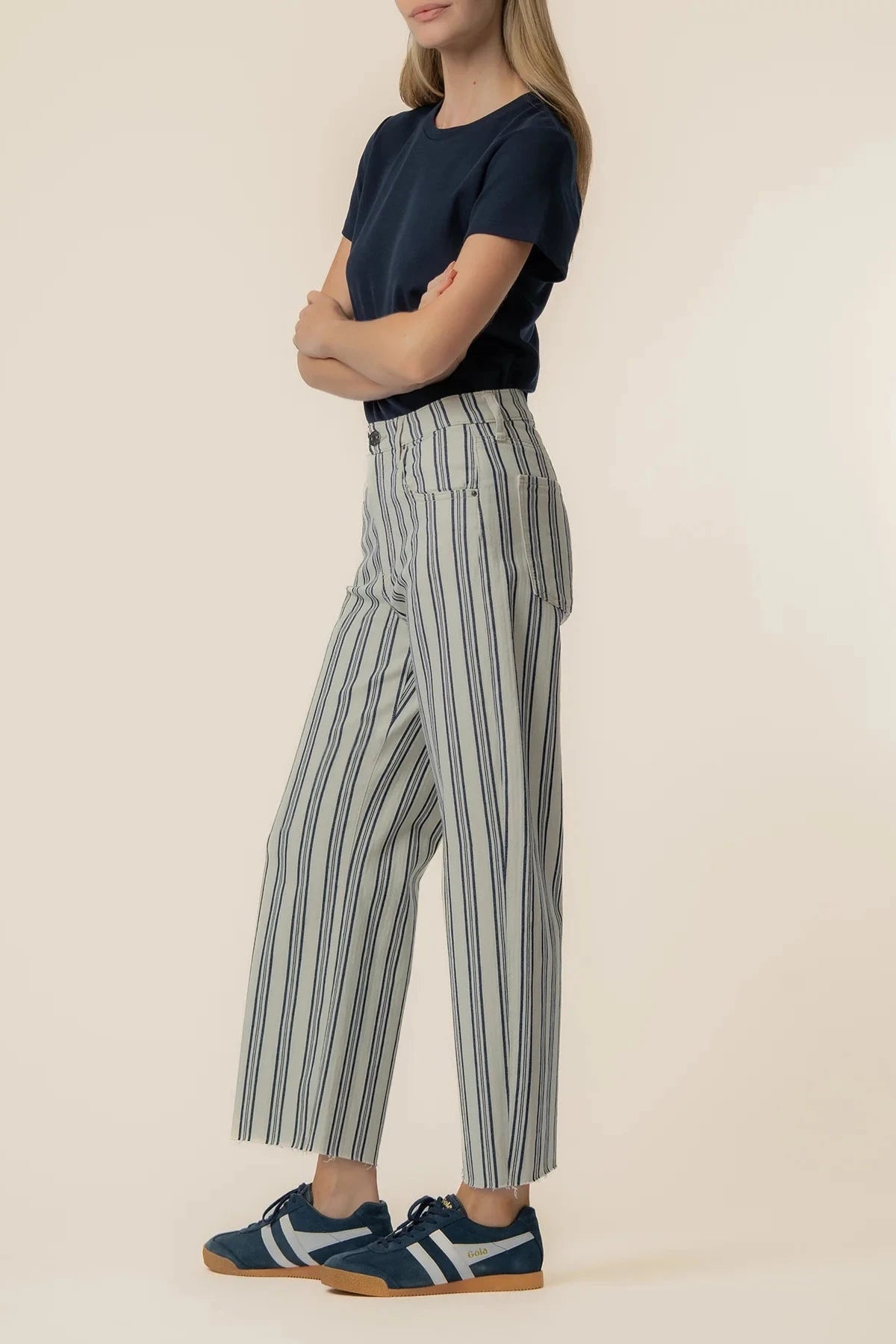 Person wearing a navy top and striped pants on a beige background