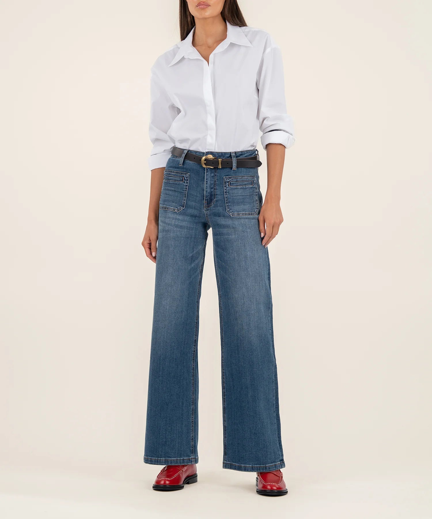 Person wearing a white shirt, blue jeans, and red shoes on a beige background