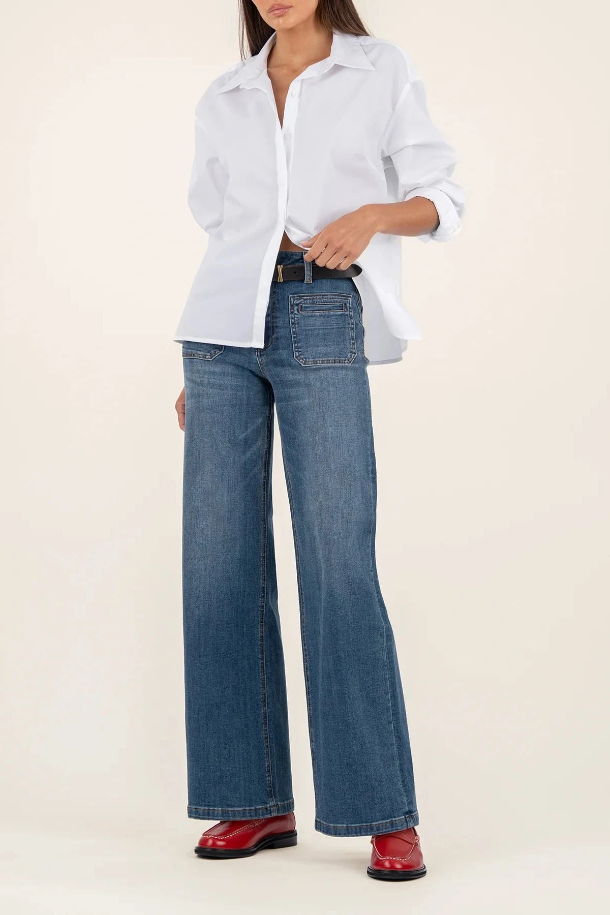 Person wearing a white shirt, blue jeans, and red shoes on a beige background