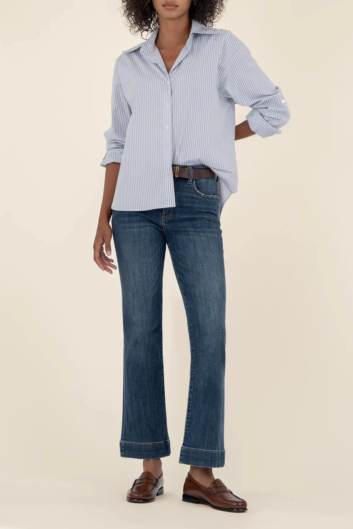 Person wearing a light blue checkered shirt, dark blue jeans, and brown shoes on a beige background