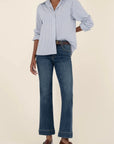 Person wearing a light blue checkered shirt, dark blue jeans, and brown shoes on a beige background