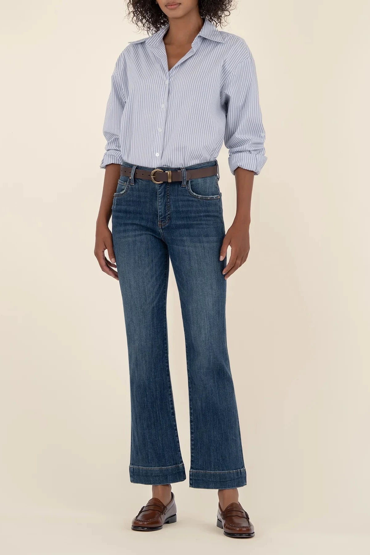 Person wearing a light blue checkered shirt, dark blue jeans, and brown shoes on a beige background
