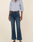 Person wearing a light blue checkered shirt, dark blue jeans, and brown shoes on a beige background