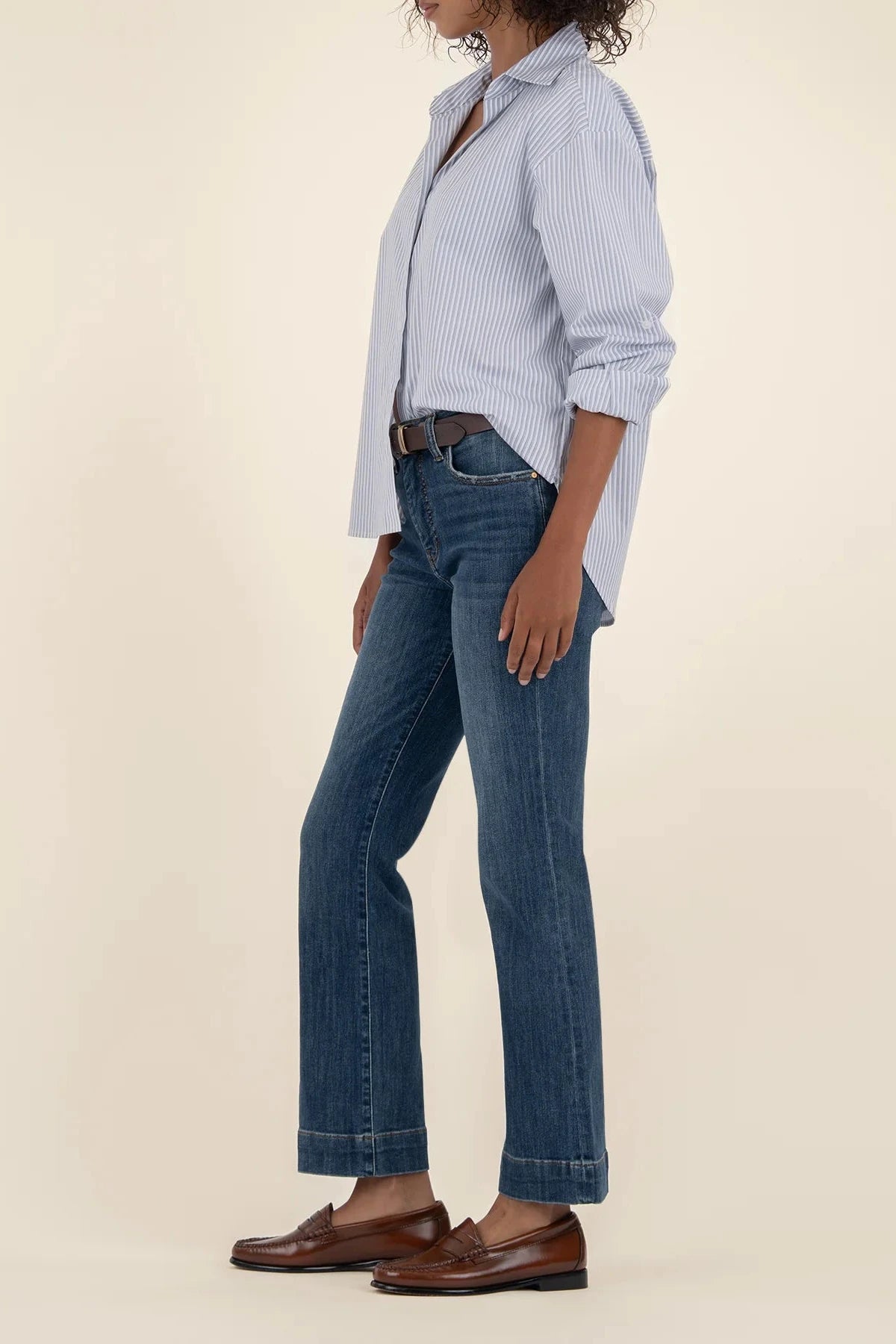 Person wearing a light blue checkered shirt, dark blue jeans, and brown shoes on a beige background
