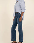 Person wearing a light blue checkered shirt, dark blue jeans, and brown shoes on a beige background