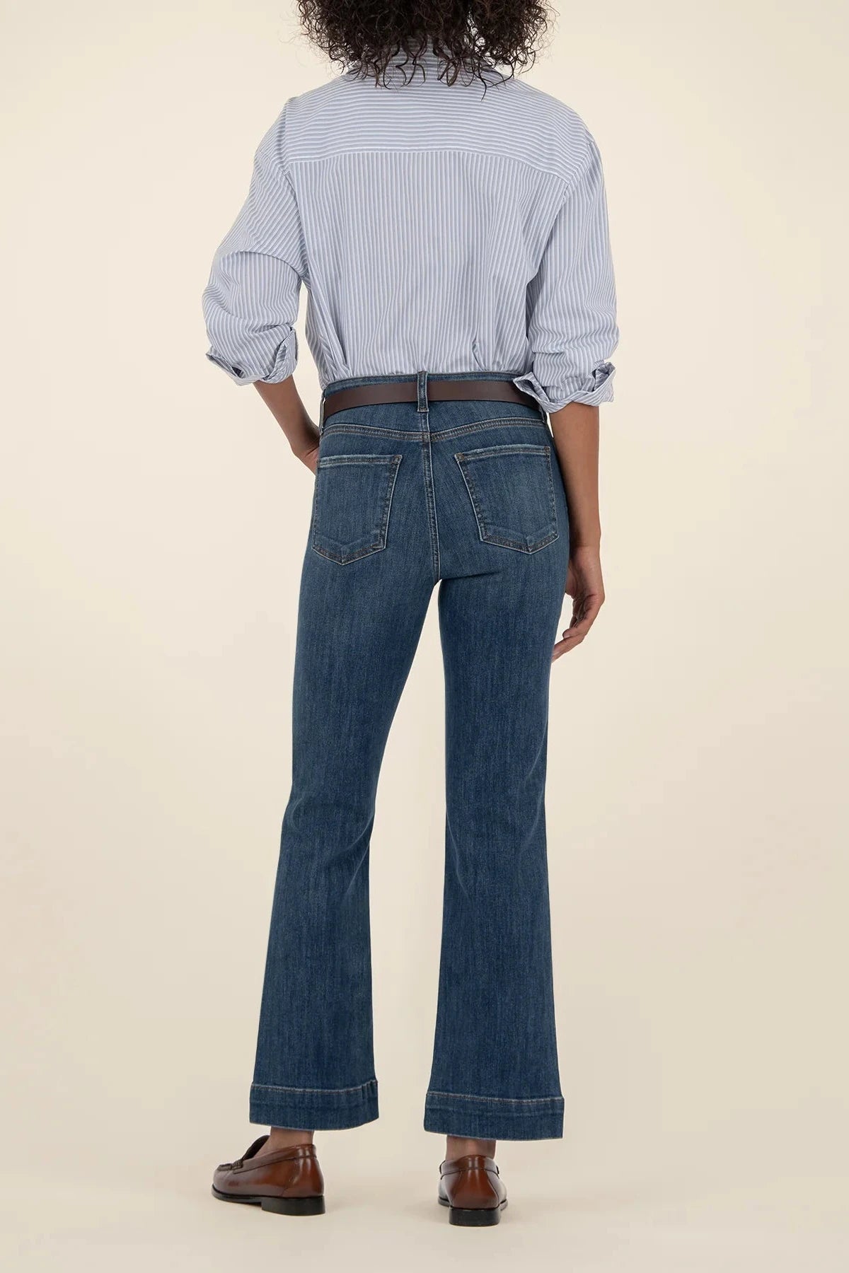 Person wearing a blue striped shirt and dark blue jeans on a beige background