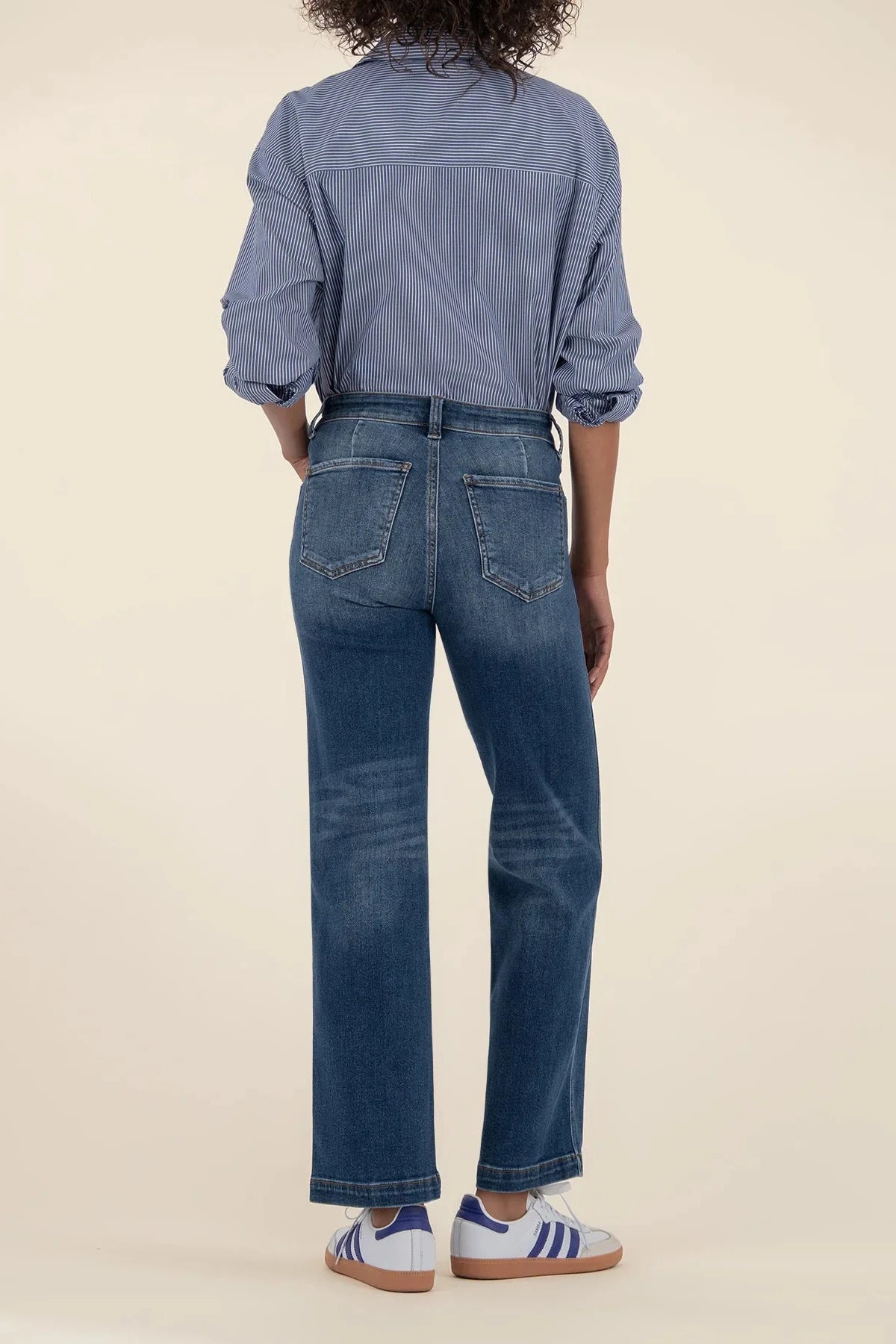 Person wearing a blue denim shirt and jeans on a beige background