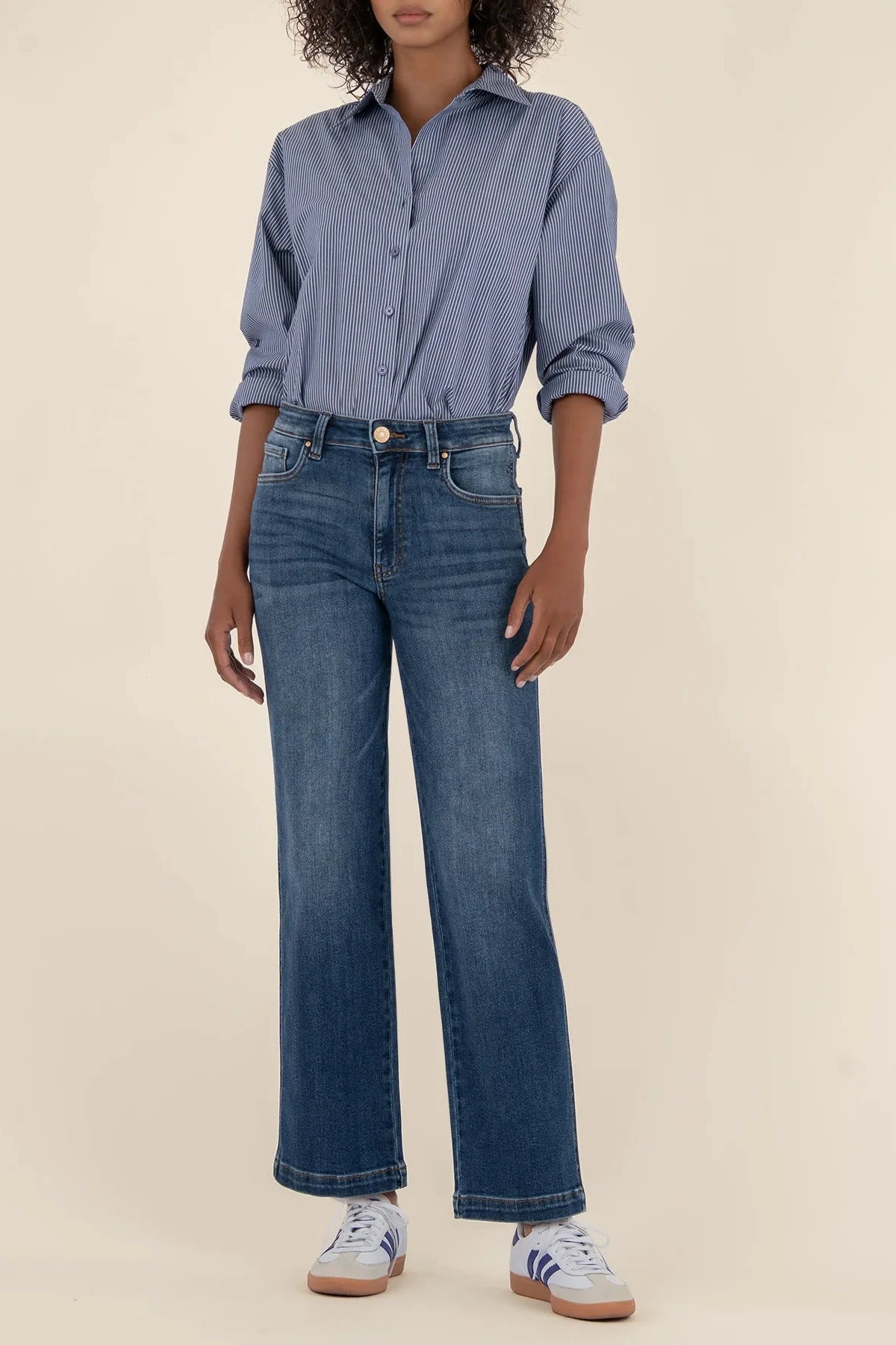 Person wearing a blue button-up shirt and jeans on a beige background